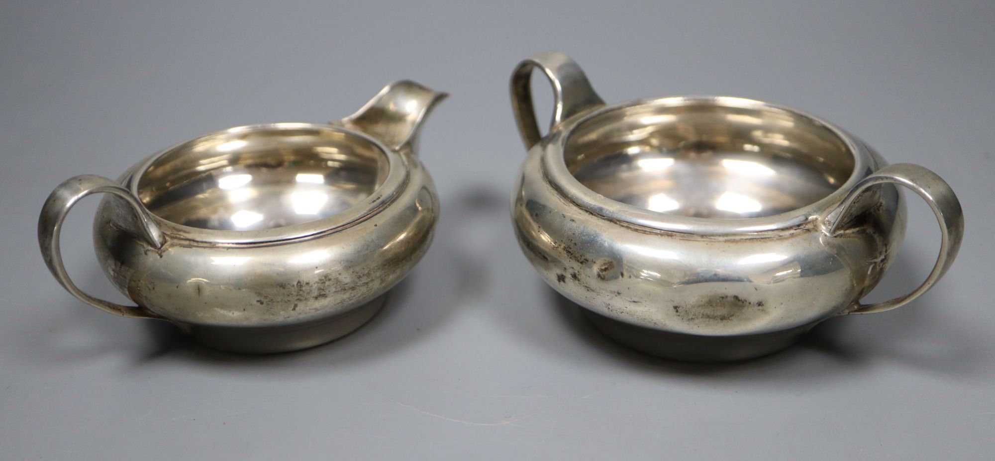 A George V silver sugar bowl and cream jug, London 1935 and a pair of Edwardian silver salt and pepper pots, London 1905,